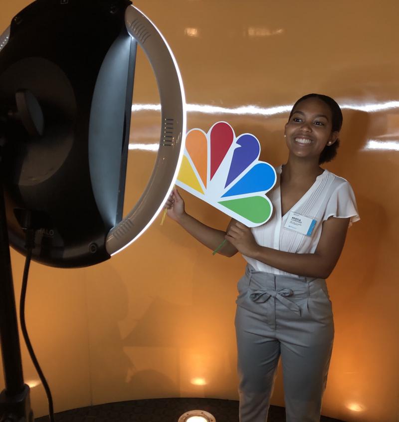Ajayla poses at a selfie station holding the NBC logo