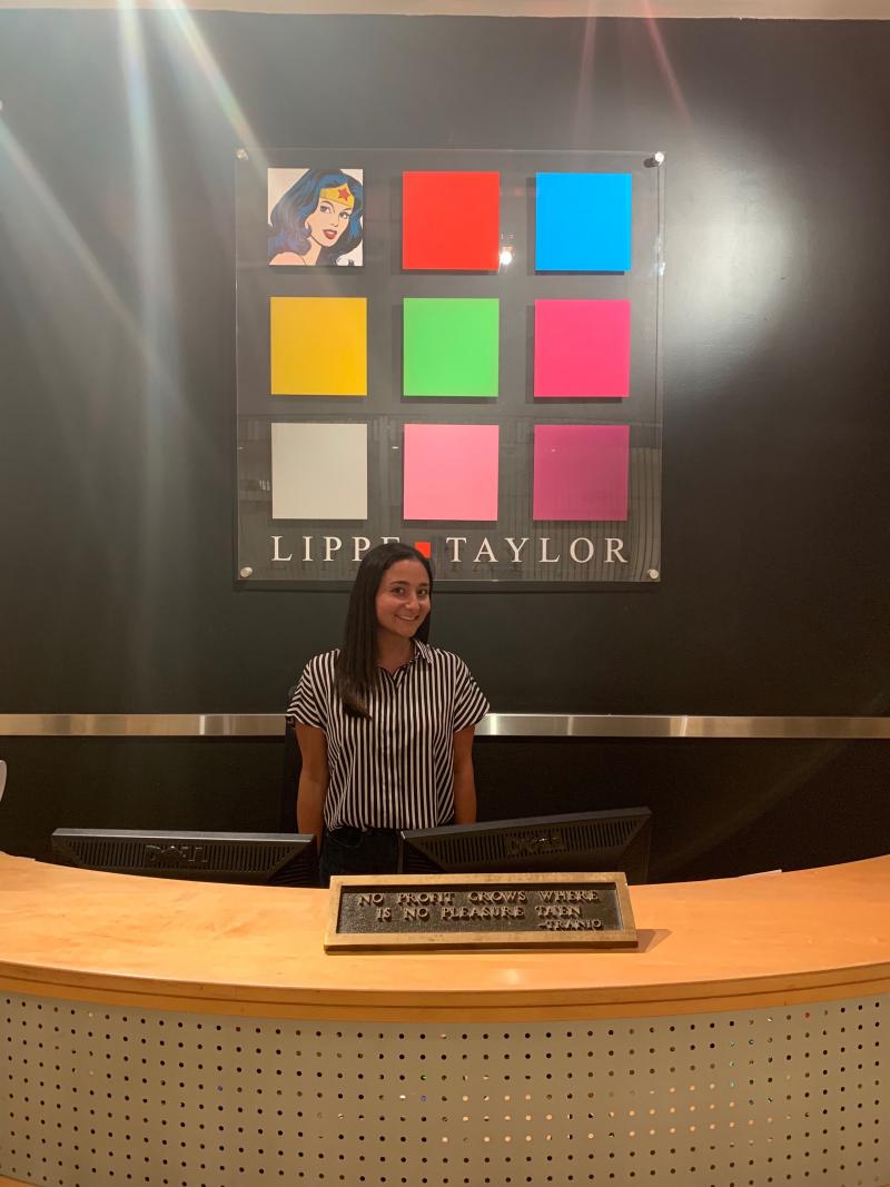 Naomi Posner posing in front of the Lippe Taylor logo