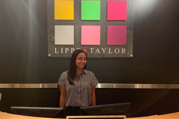 Naomi Posner posing in front of the Lippe Taylor logo